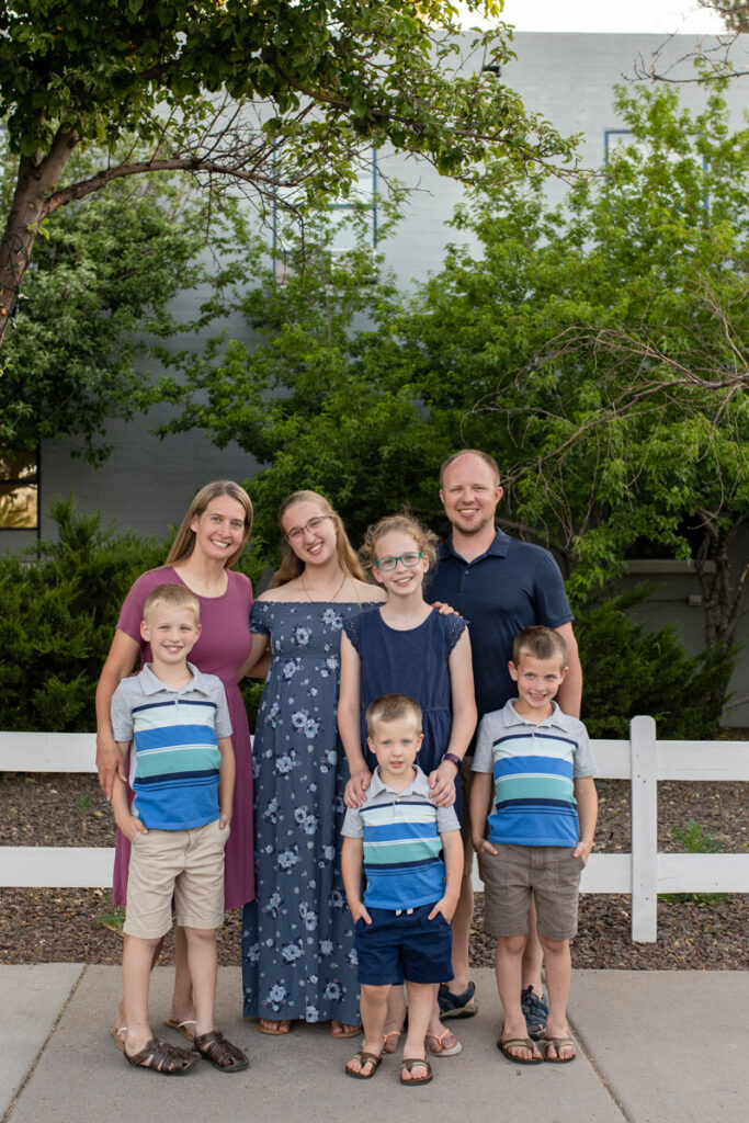 Family of 7 smiles in front of white fence.