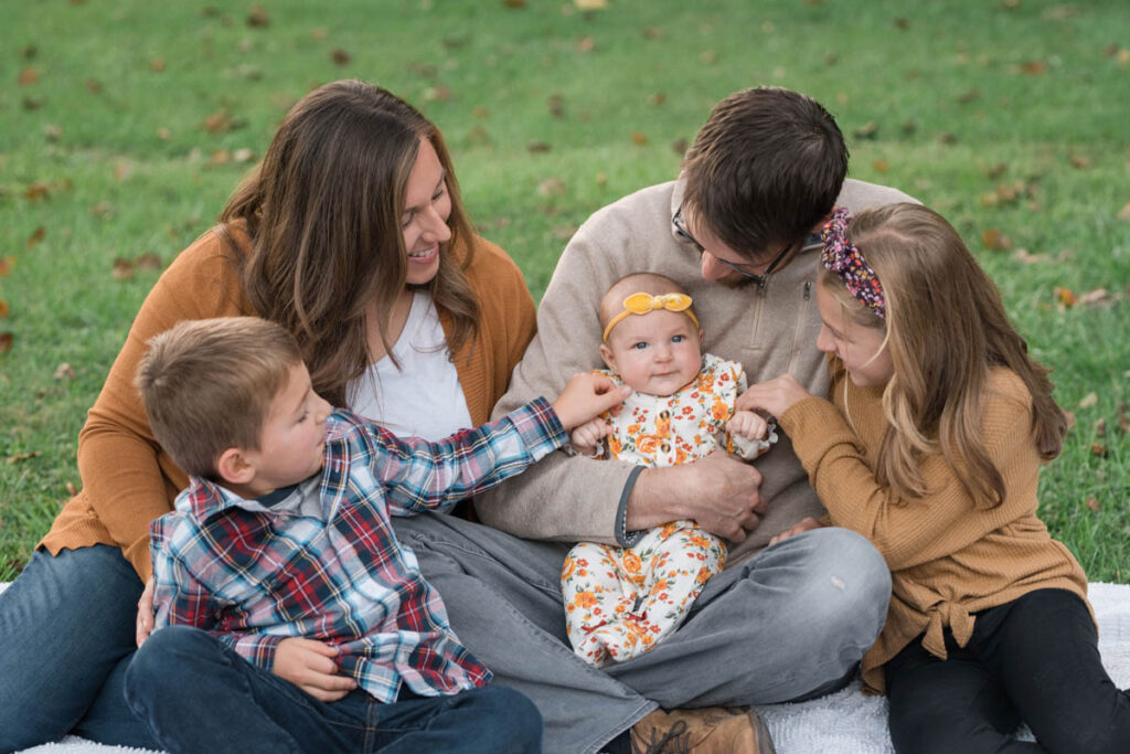 Family is sitting on a white blanket playing with baby.