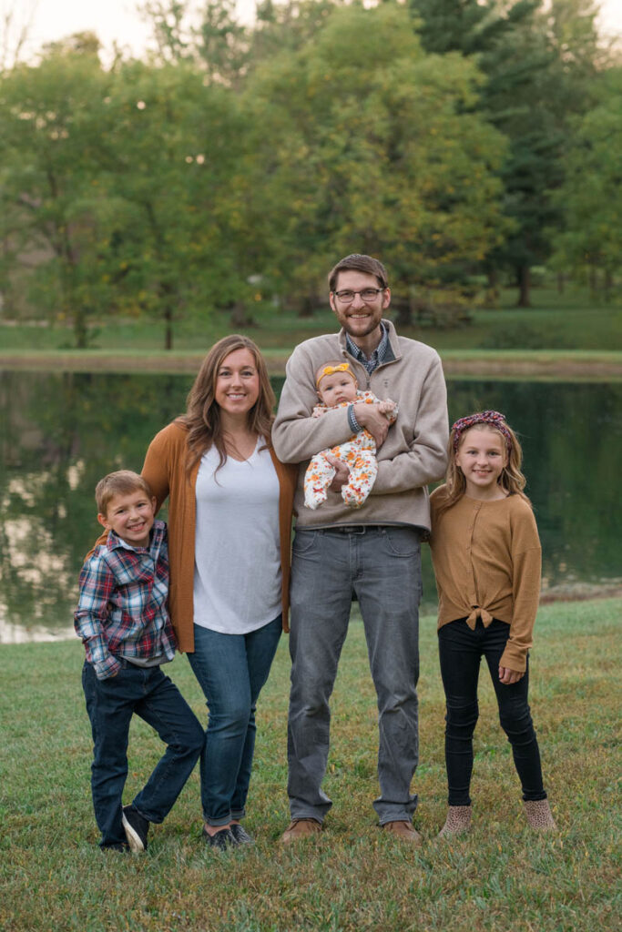 Family stands in front of a pond smiling.