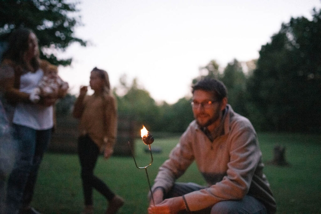 Father helping roast marshmallows with family over campfire.