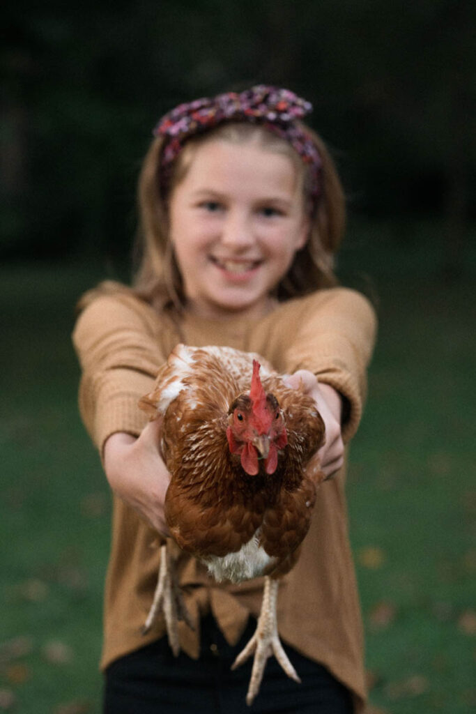 Girl holds red-brown colored chicken out in front of her while smiling.