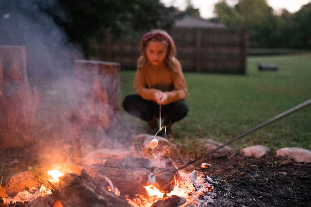Girl roasting marshmallow over campfire.