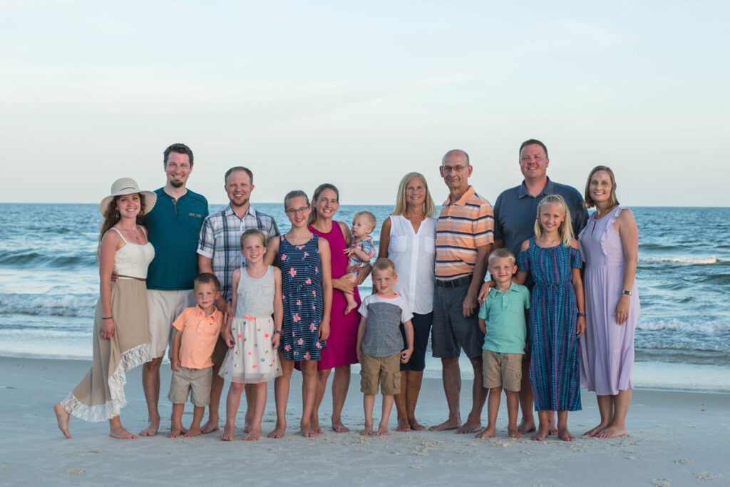 Large family stands on the beach smiling at sunset.