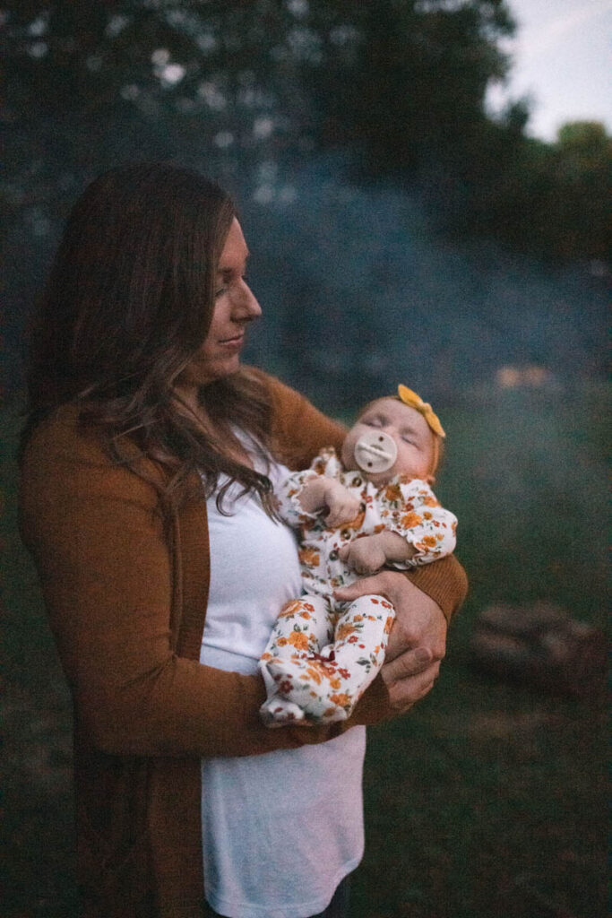 Mother holds sleeping daughter in the late evening light.