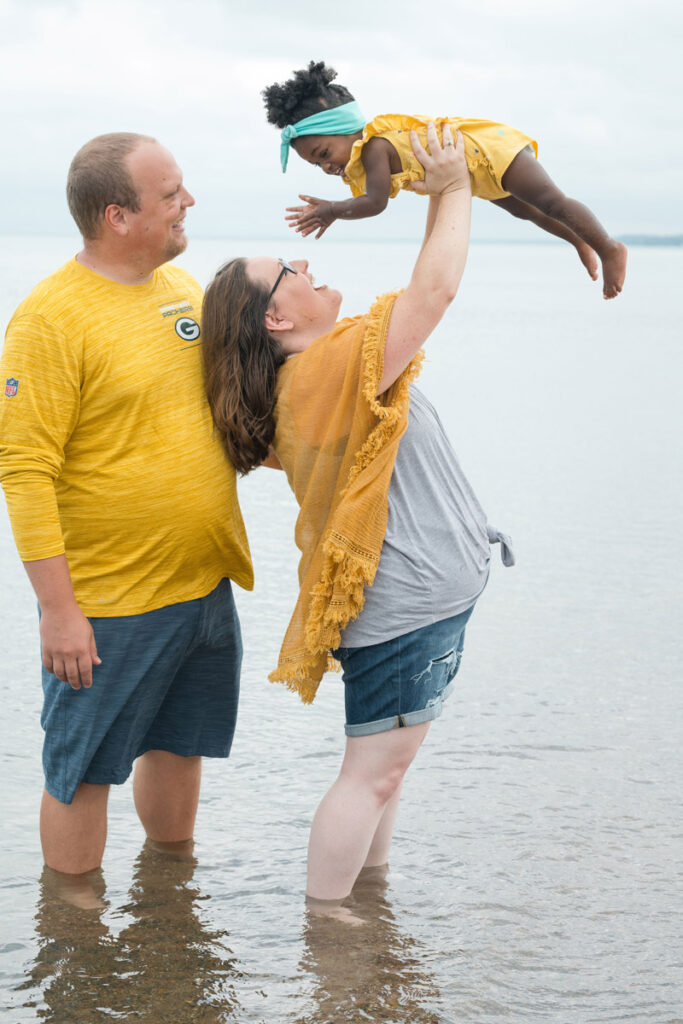 Mother and father lift up laughing daughter while standing in the water.