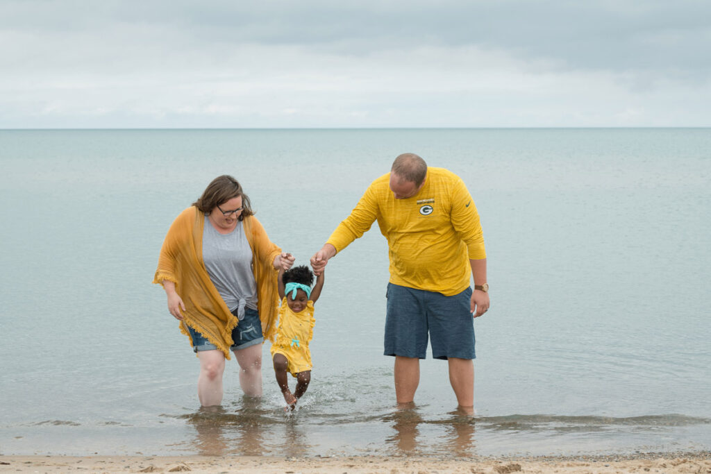 Parents hold daughter's hands and swing her in the lake water.