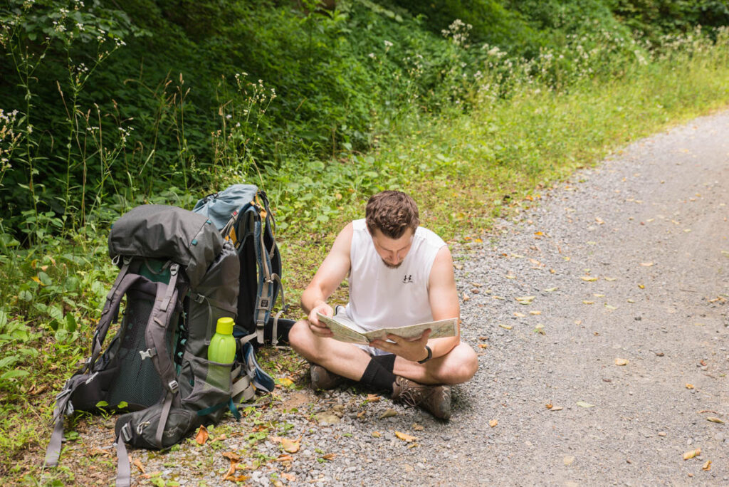 Man is looking at a map during his hike on the side of a trail.