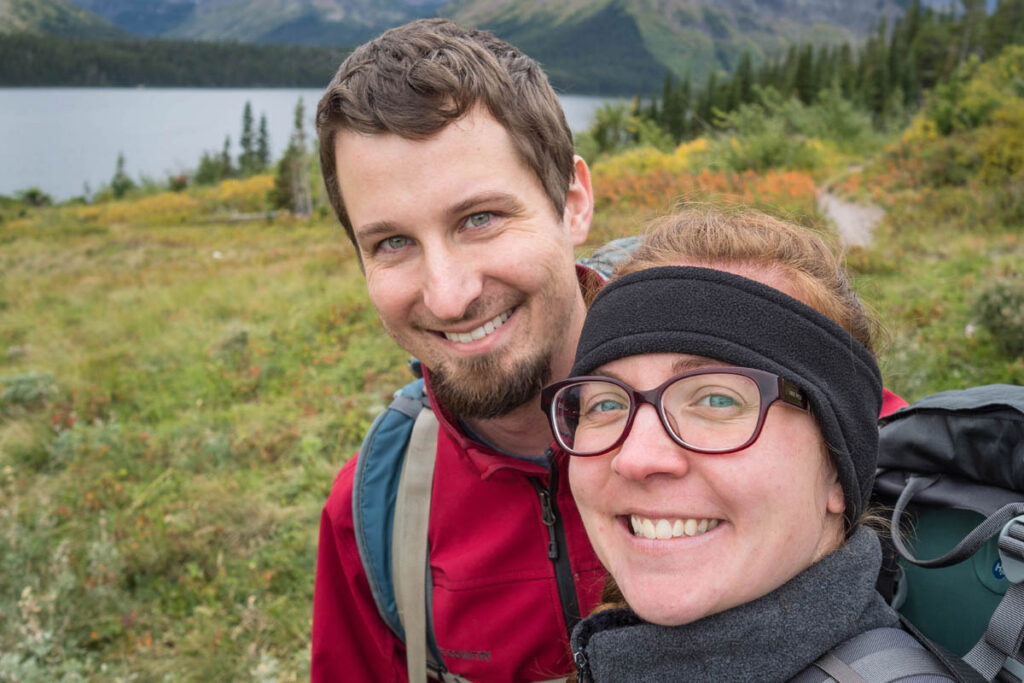 Couple smiles while hiking on mountain trail at Glacier National Park.