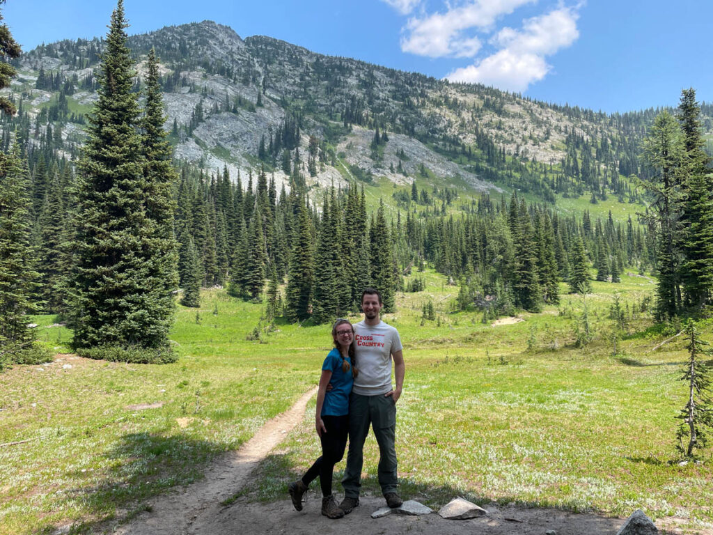 Couple hugs in the middle of a valley surrounded by trees at North Cascades National Park.