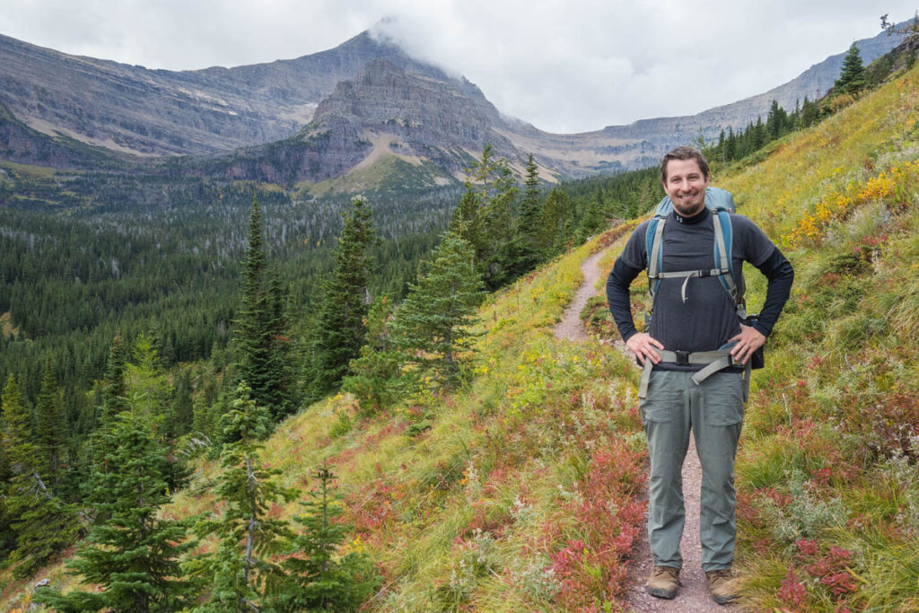 Man smiles with pack on his back on a mountainous trail.