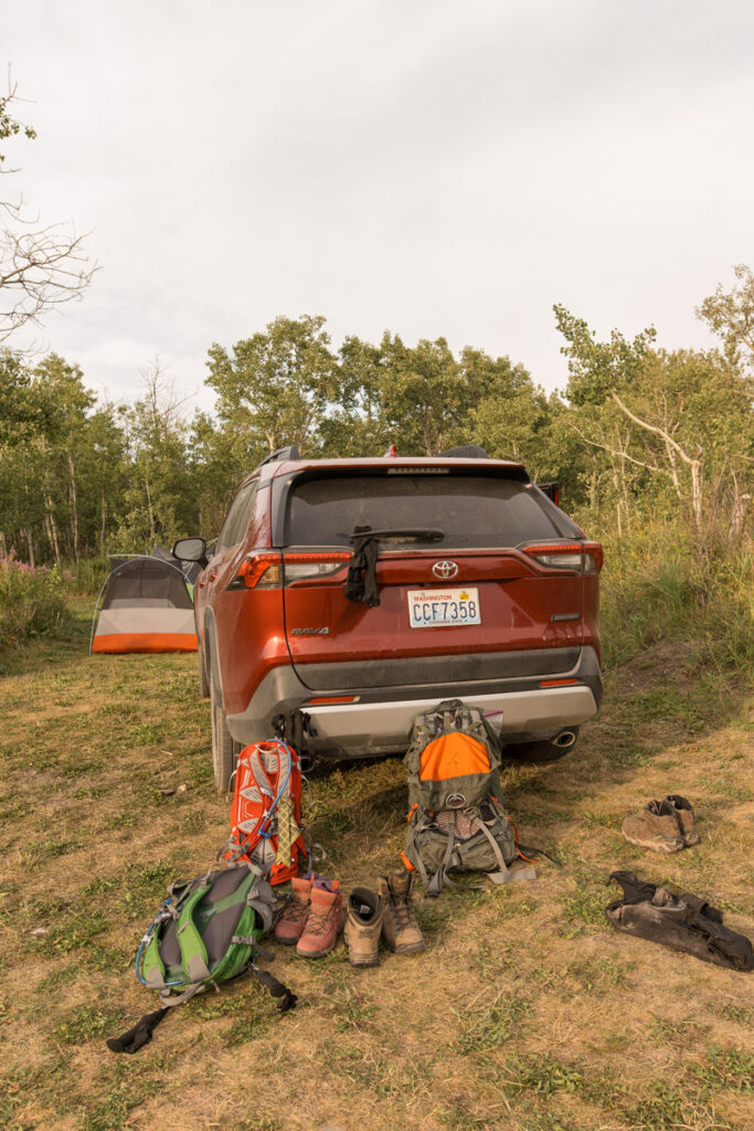 Packs sit by red car at campground.