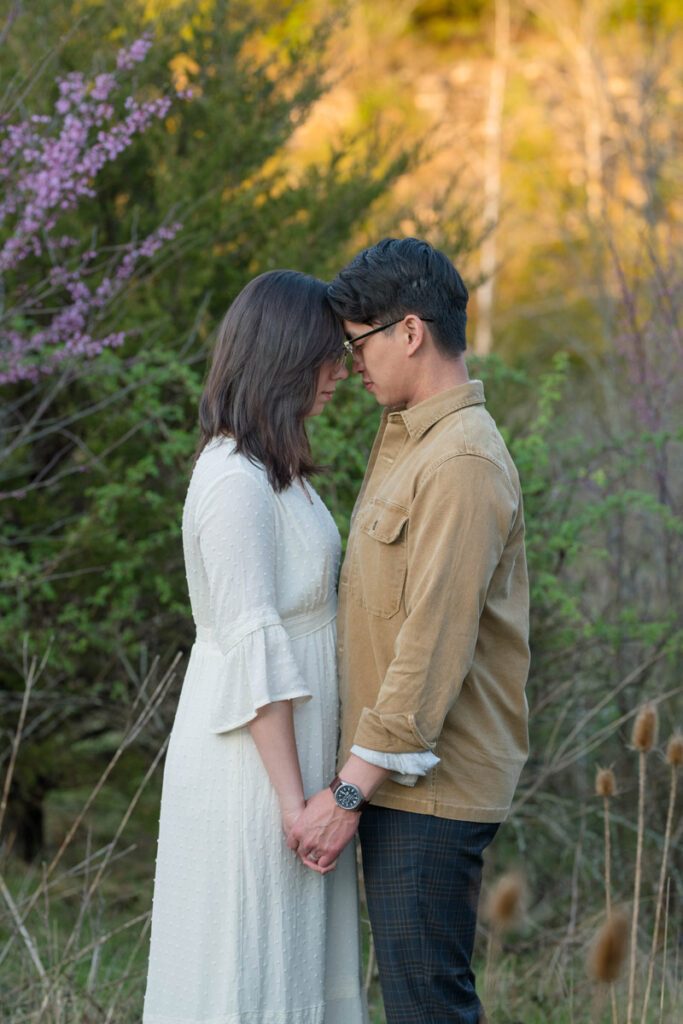 Couple rests their heads together surrounded by trees at sunset.