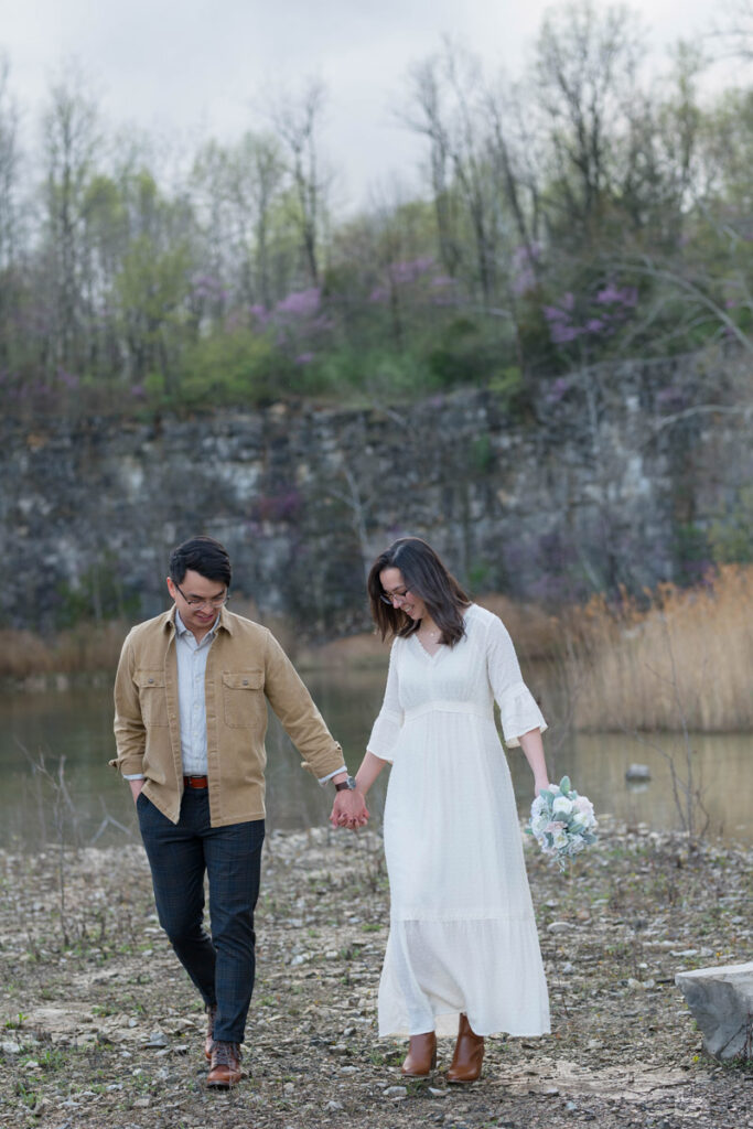 Couple walks together holding hands while woman holds her bouquet.