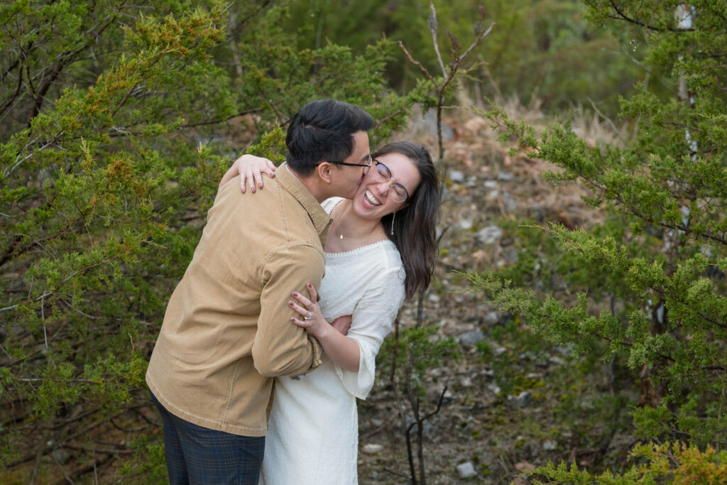 Woman laughs while man kisses her cheek.