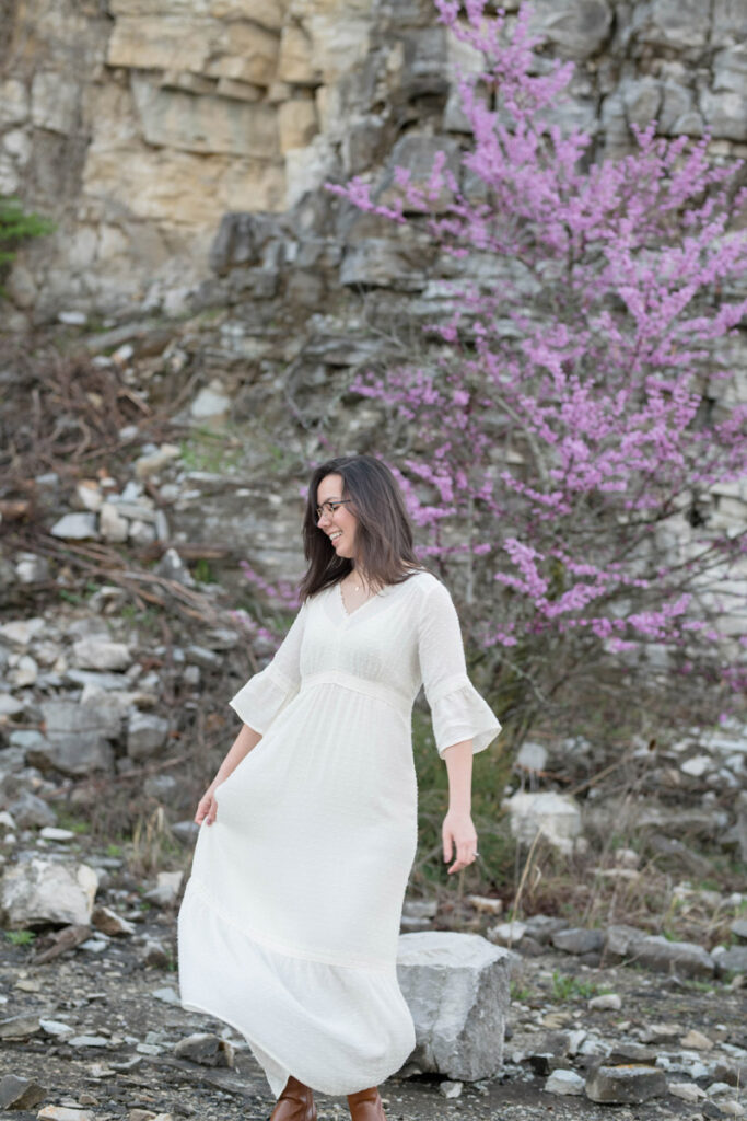 Woman twirls in her white dress in front of purple flowering tree.