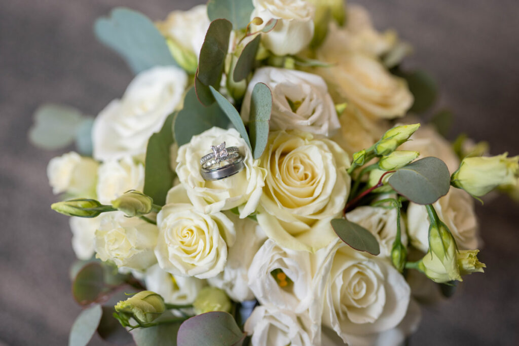 Wedding rings resting on bride's bouquet of white roses.