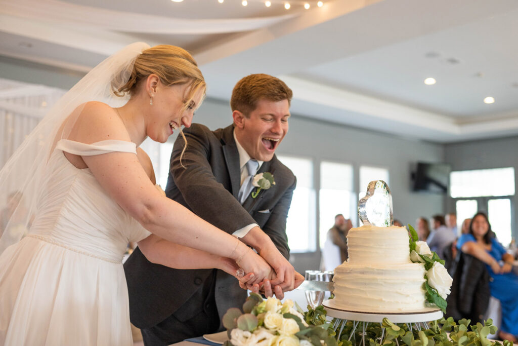 Groom and bride laughing while cutting the cake together.