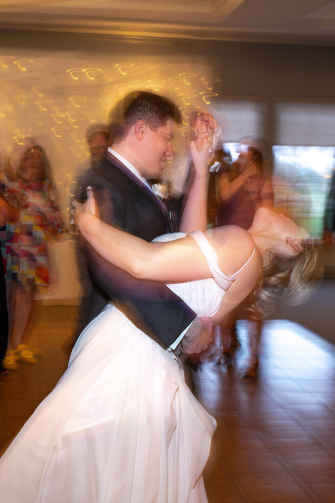 Groom dips bride while dancing at wedding reception.