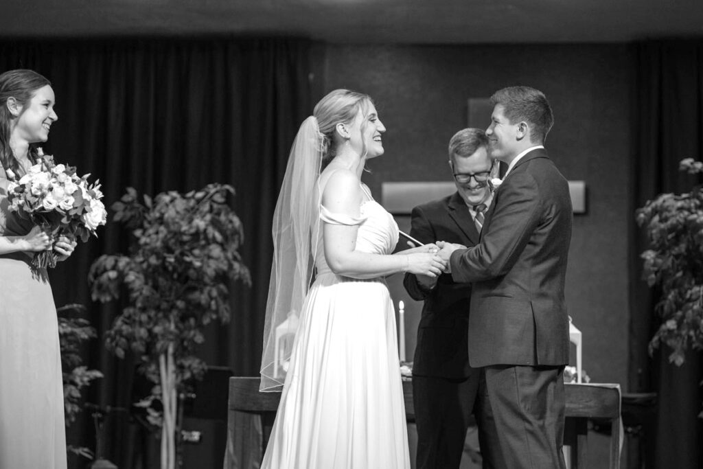 Couple laughs while exchanging rings and vows during ceremony.