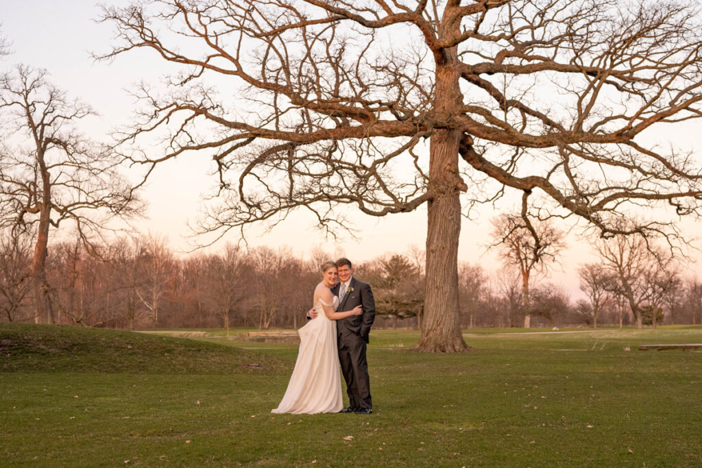 Bride and groom standing on the golf course at the Golf Club of Indiana next to a large tree.