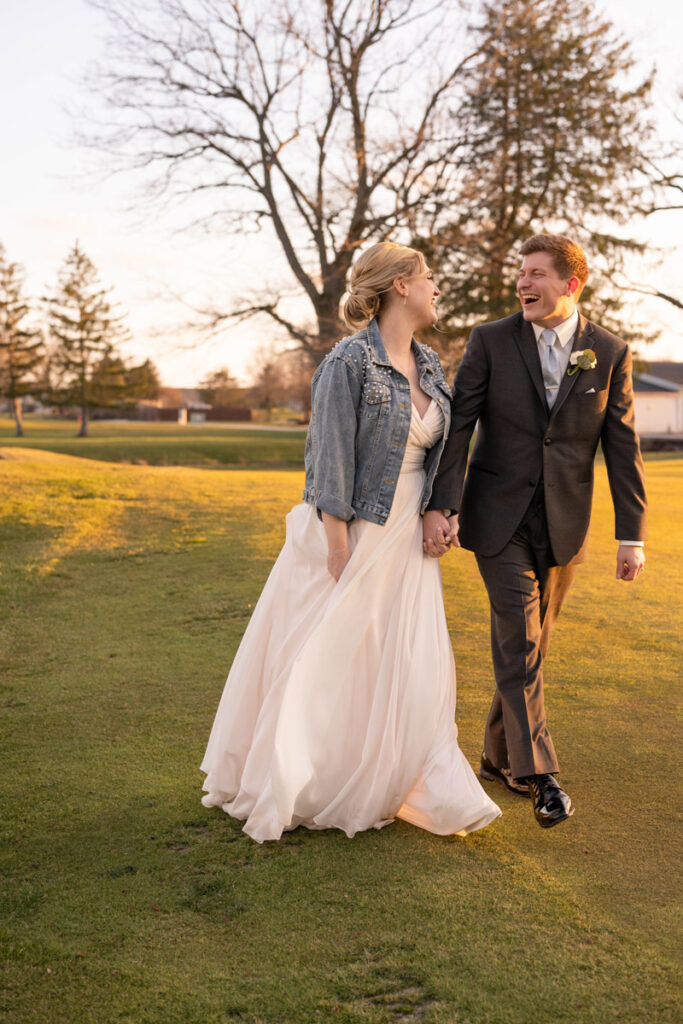 Groom and bride holding hands while walking at gold course at The Golf Club of Indiana at sunset.