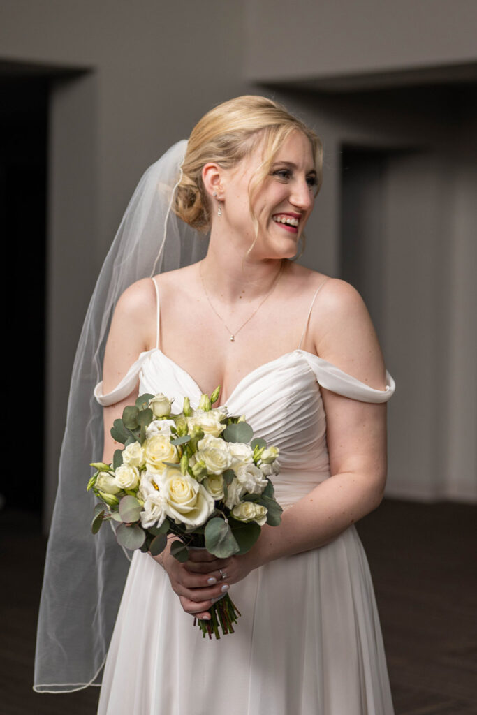 Bride smiling and laughing while holding her bouquet and looking to the right.