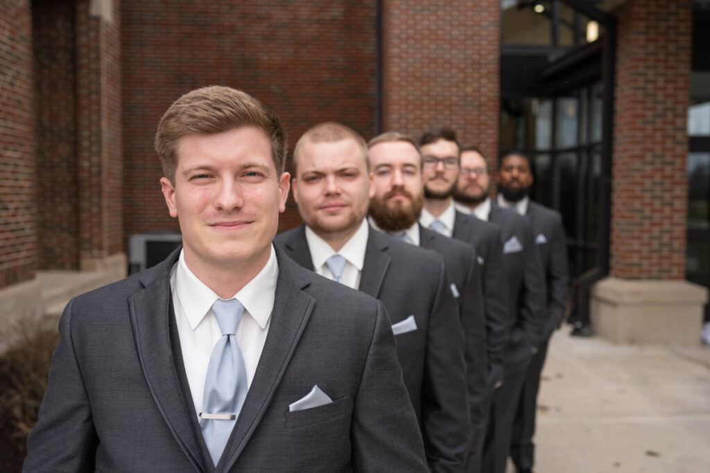 Groom with out of focus groomsmen in a diagonal line behind him.