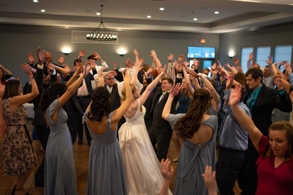 Bride and groom dancing with all their guests with hands raised at the reception.