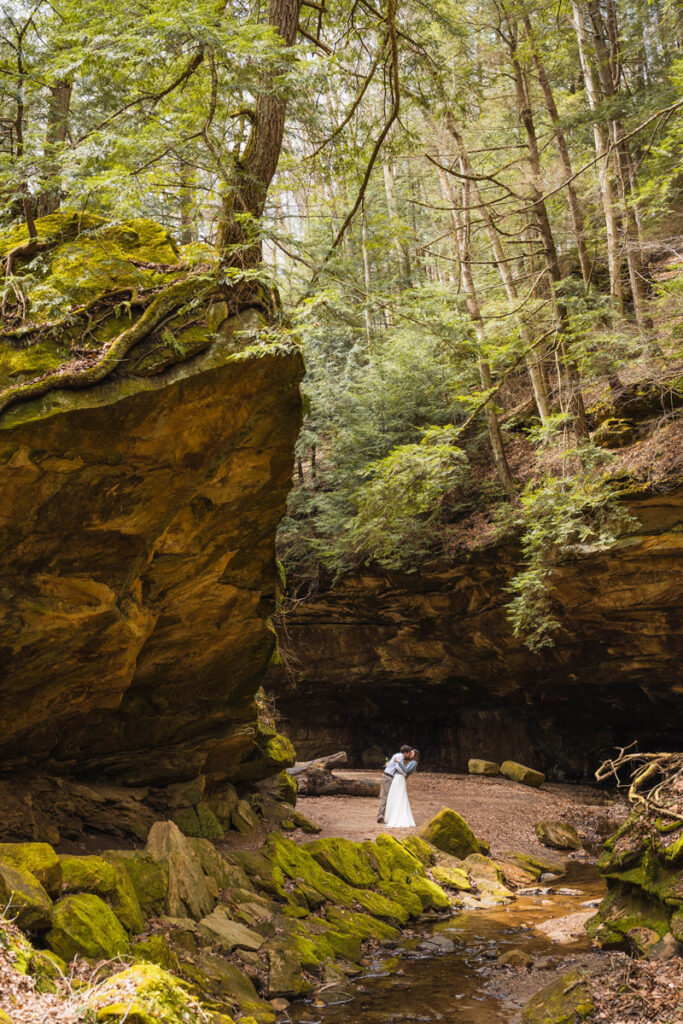 Newlyweds share a dip kiss next to a huge boulder in a gorge.