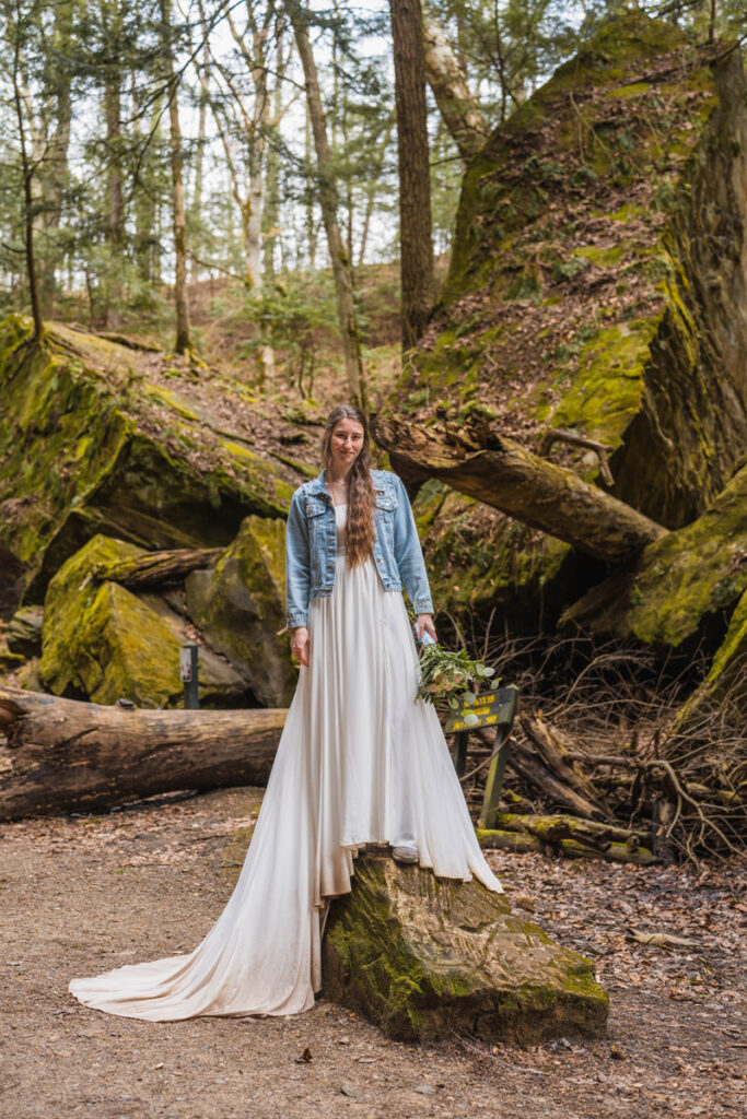 Bride smirks while standing on large rock.