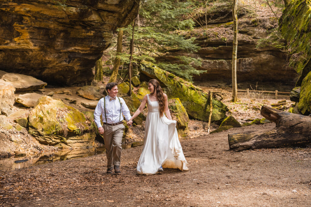 Newlyweds running through a state park while holding hands.