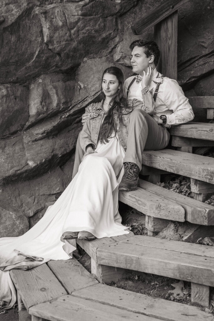 Couple sits on steps in their wedding attire looking away.