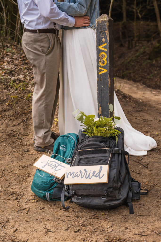 Couple embrace next to trailhead and packs.