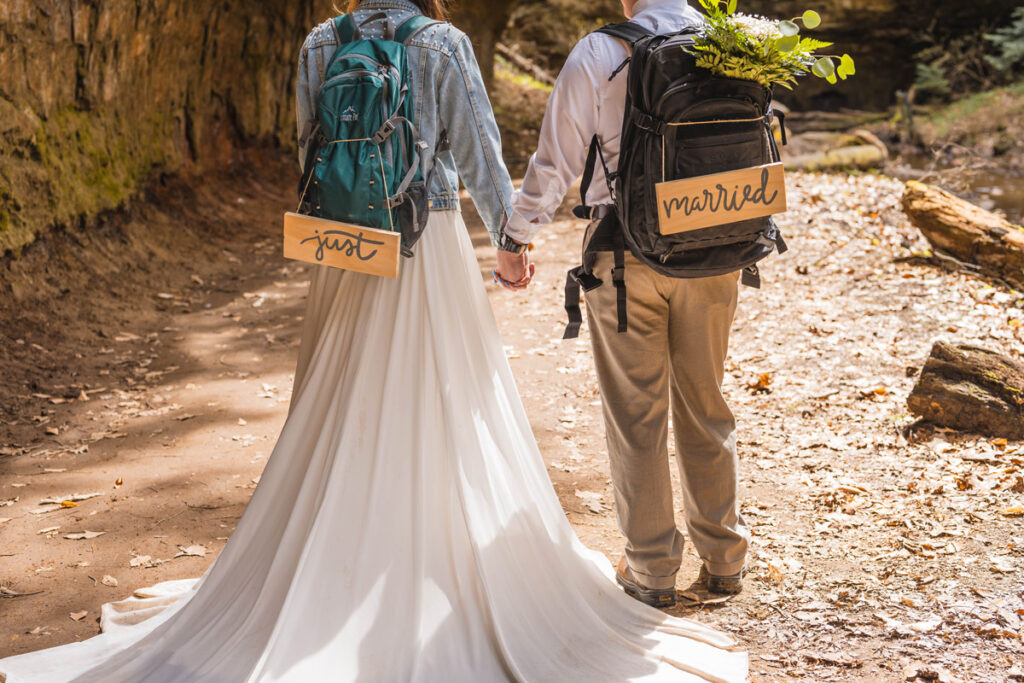 Backs of bride and groom wearing their packs with just married signs.