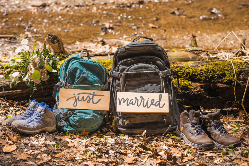 Backpacks with just married signs rest in the sun again a mossy logs next to hiking books.