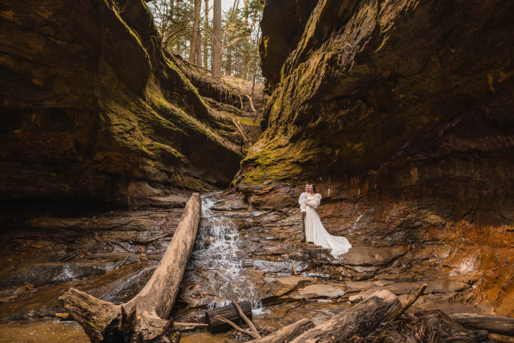 Bride and groom standing in a gorge hold one another close and look up.