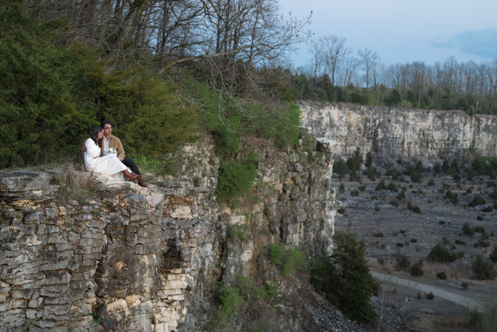 Bride and groom hold each other close and look over rocky cliff together.