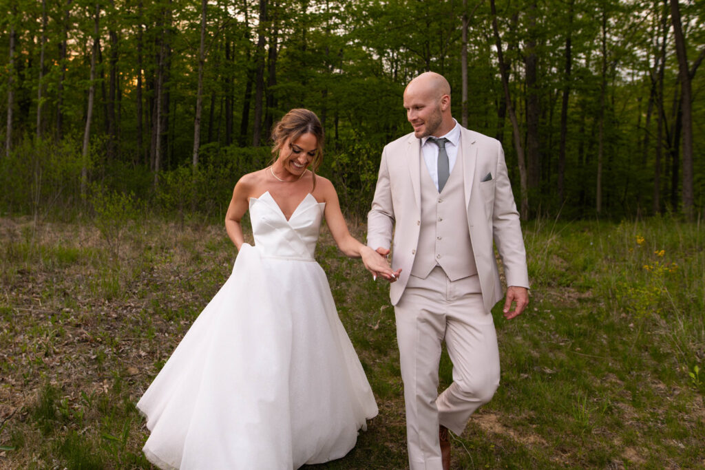 Bride and groom holding hands and smiling as they walk in the forest.