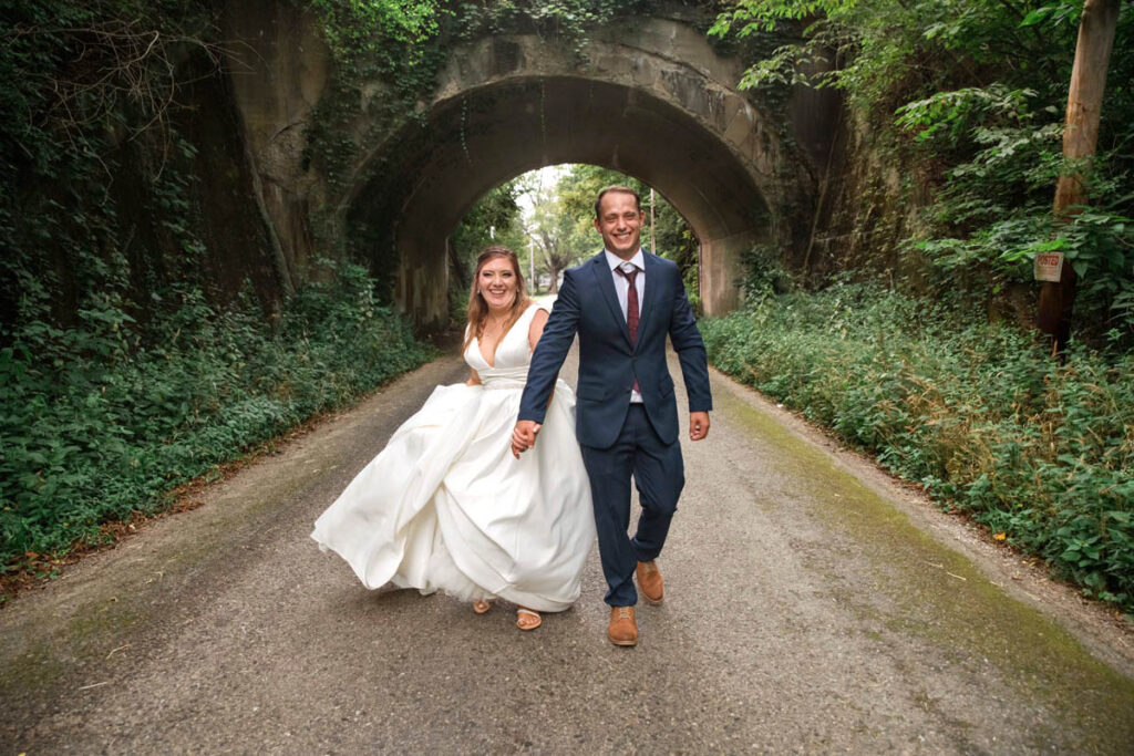 Groom and bride walk in front of bridge laughing.