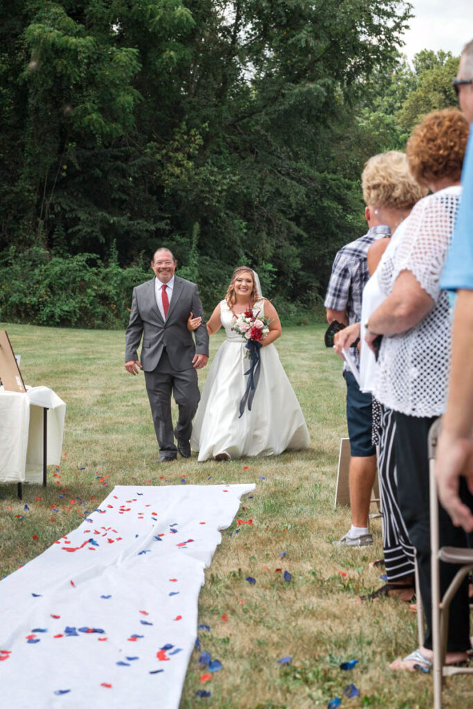 Father walks bride down the aisle during her outdoor wedding ceremony.
