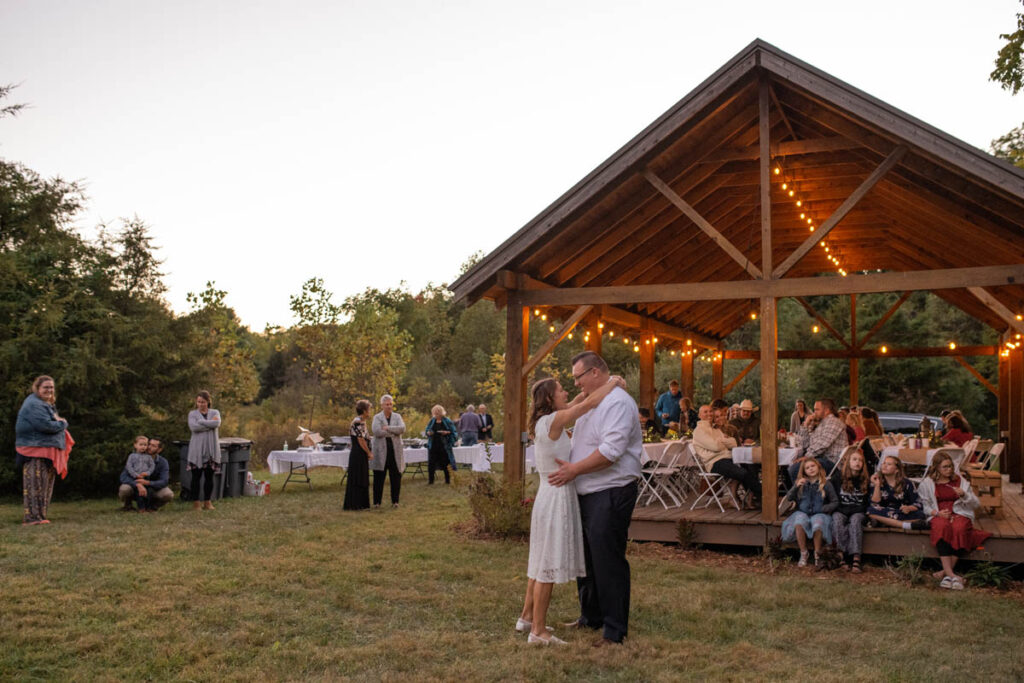Couple shares their first dance outside near a pavilion with their guests.