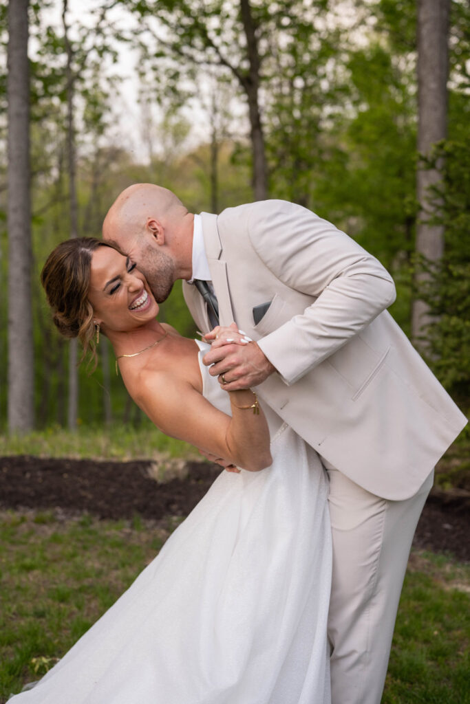 Groom kisses bride on cheek while she leans back laughing.
