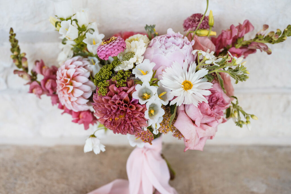 Pink and white floral bouquet rests again a white stone wall.