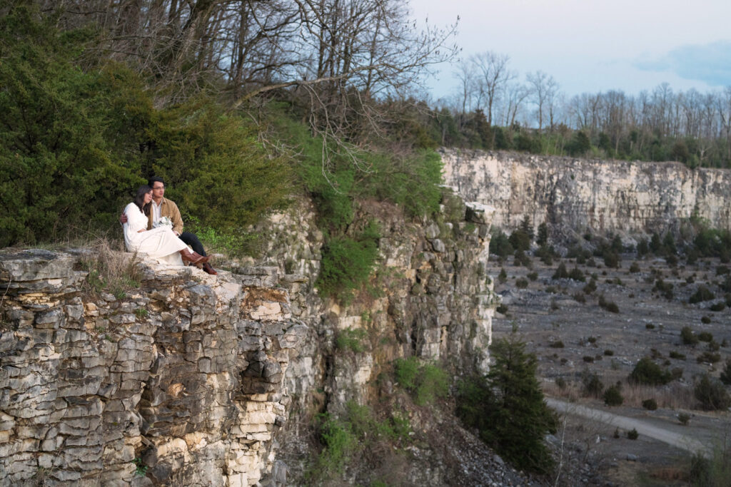 Bride and groom sit on edge of rock quarry looking off into the distance.