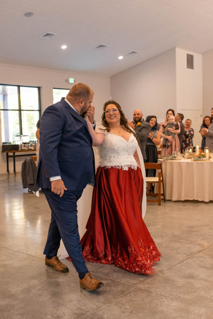 Groom kisses bride's hand as they enter reception space.