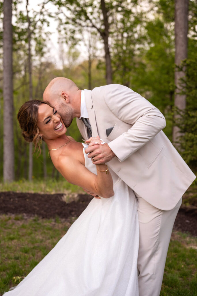 Groom kisses bride's cheek while she laughs.