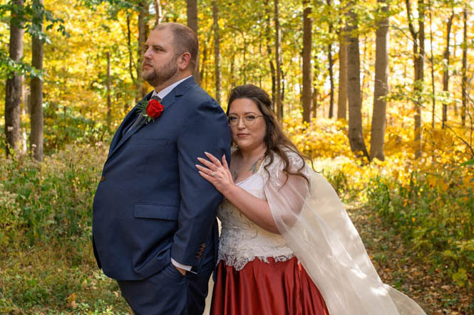 Bride looks serious while groom looks away standing in forest next to Owl Ridge Wedding Venue.