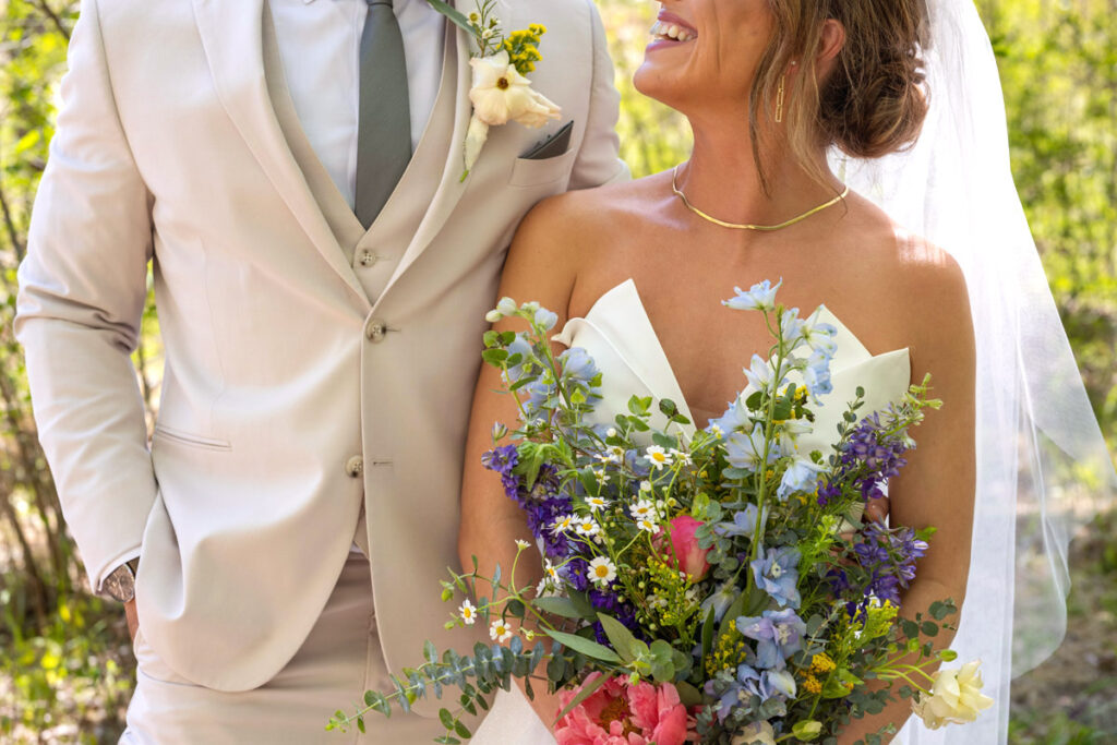 Bride smiles while looking up at groom and holding wildflower bouquet.