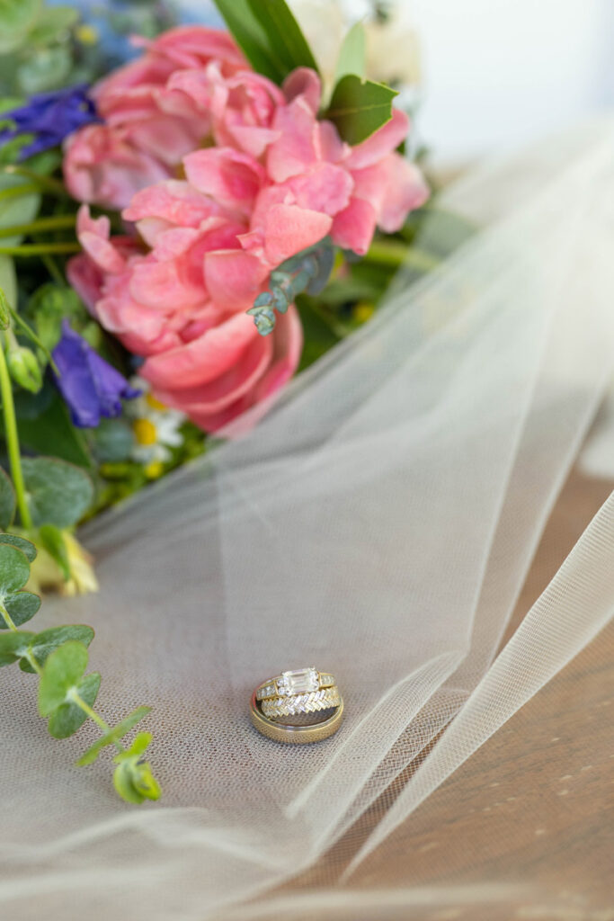 Wedding rings rest on veil in front of spring wildflower bouquet.