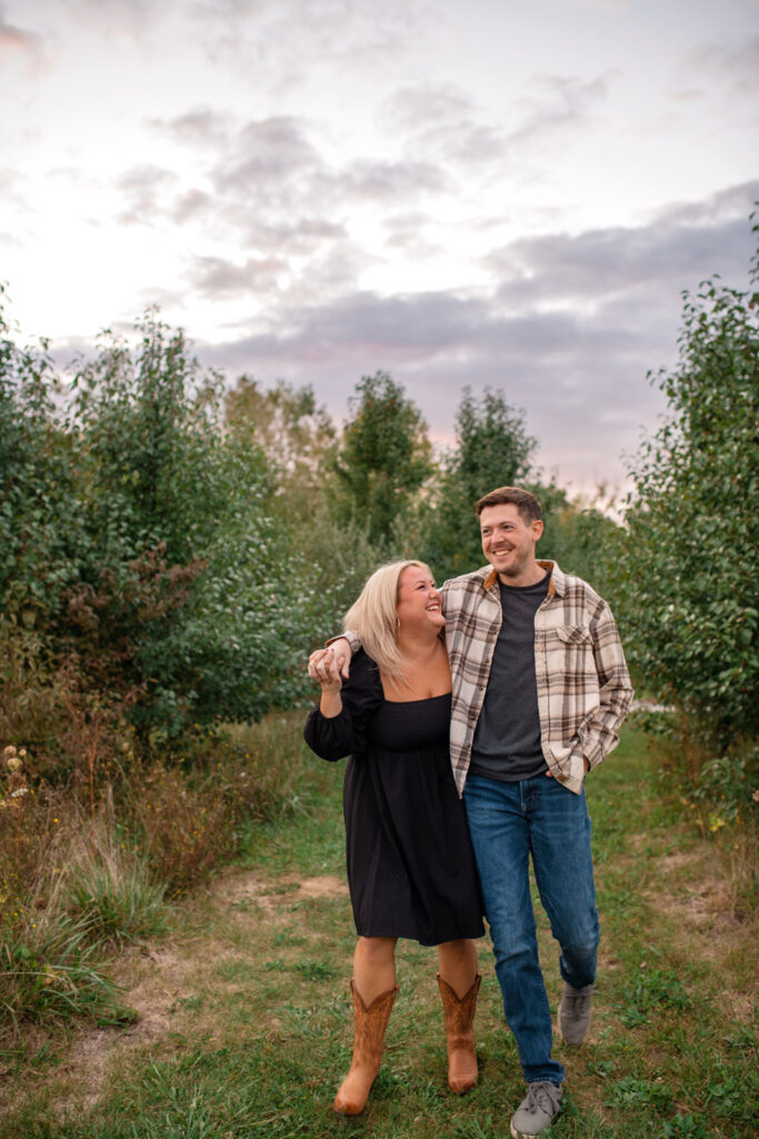 Couple stroll through a tree lined area while laughing.